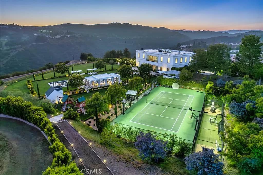 Aerial view of luxury estate with illuminated tennis court and manicured landscaping